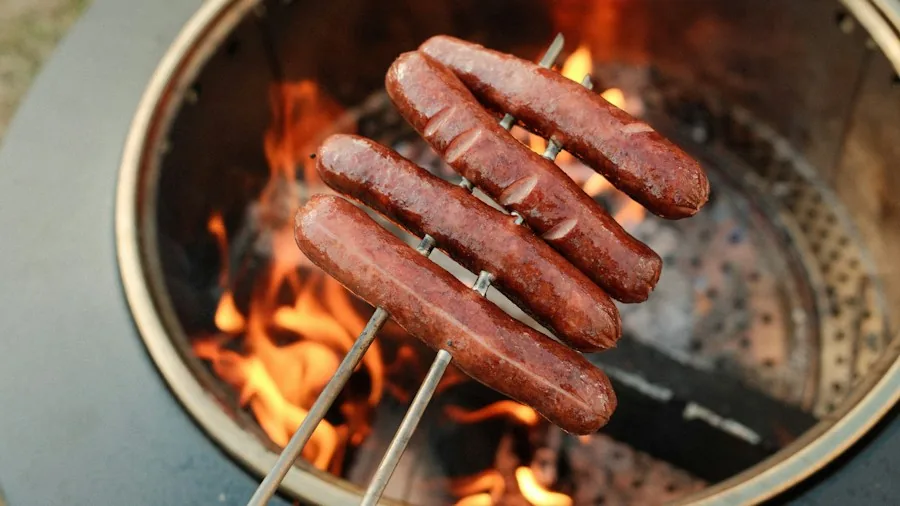 People gathered around a backyard fire pit preparing food on grill grates during evening