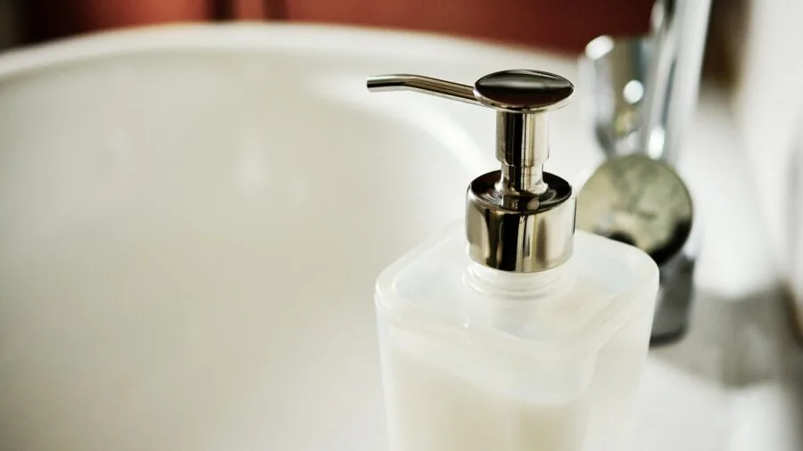 Person maintaining personal grooming tools at bathroom sink with cleaning brush and water